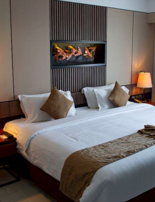 This image shows a well-lit hotel room with a large bed, two side tables with lamps, wall decor, and a window with curtains.