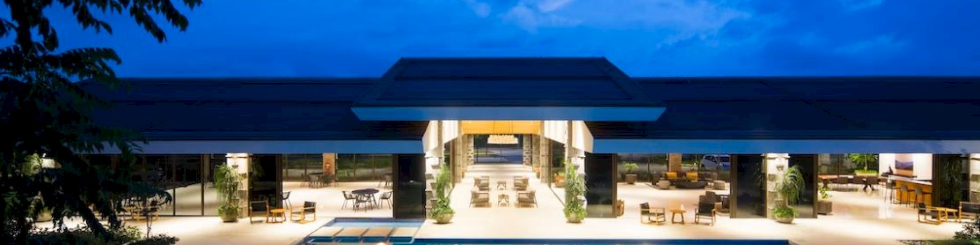A luxurious outdoor pool area at night in front of a large, modern building with an open, illuminated interior.