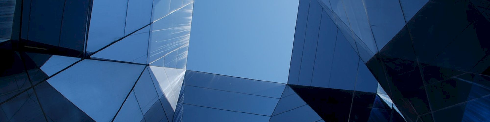 The image shows an abstract architectural structure with reflective glass surfaces forming a geometric pattern, creating a view of the blue sky.