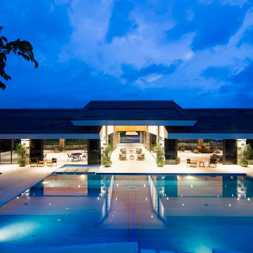 A luxurious outdoor swimming pool with a modern building in the background, set against a serene evening sky.