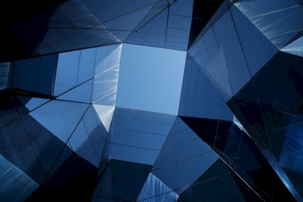 The image shows a view looking up through a geometric structure made of reflective glass panels, creating a modern architectural design.