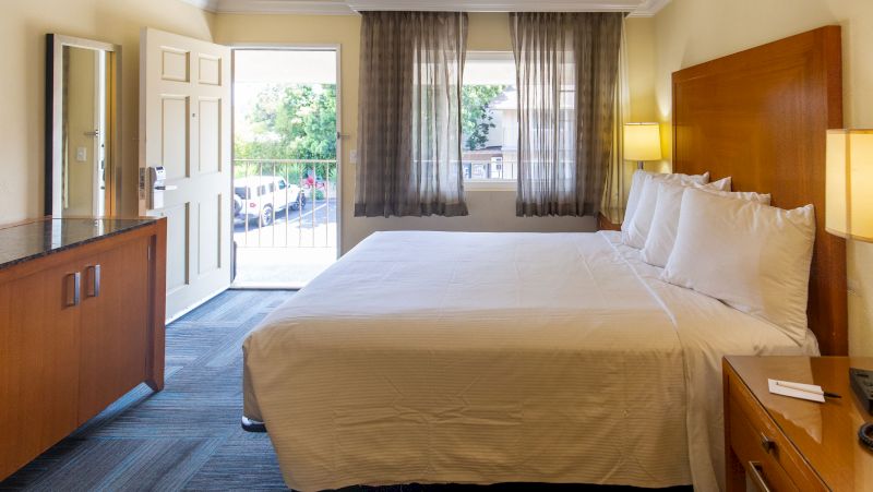 A hotel room with a large bed, wooden nightstand and dresser, and a door leading outside.