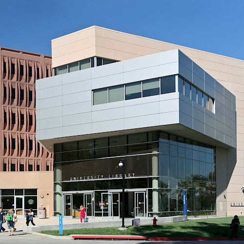 This image shows a university library building with modern architecture, featuring large glass windows and connected to other campus structures.