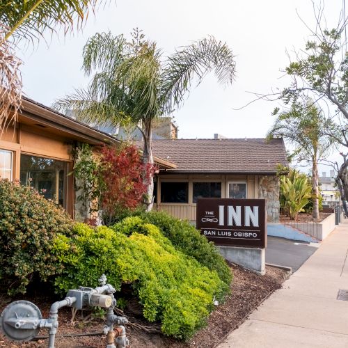 The image shows the exterior of a quaint inn with a sign reading 