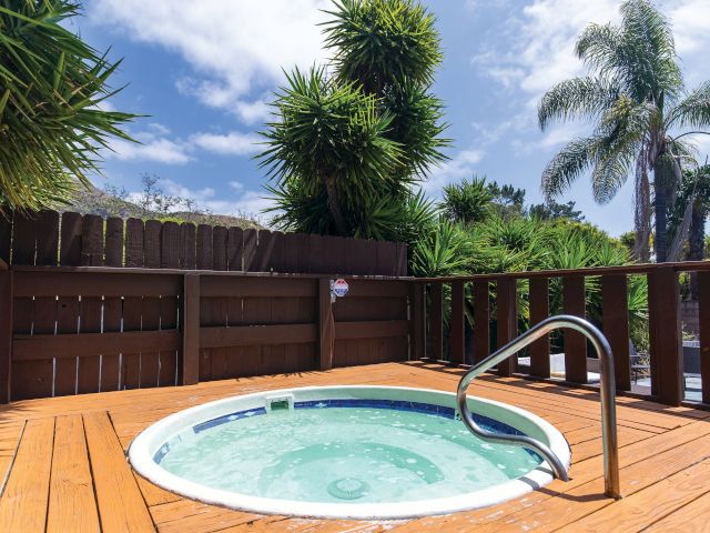 A round hot tub on a wooden deck surrounded by a fence and tropical plants.