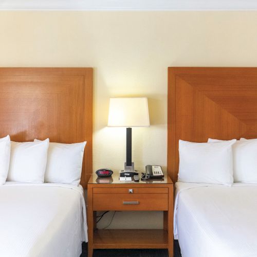 The image shows a hotel room with two beds, a nightstand between them, a lamp, and a telephone on the nightstand.