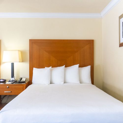 The image shows a hotel room with two beds, a nightstand, a lamp, a phone, and a framed picture on the wall.