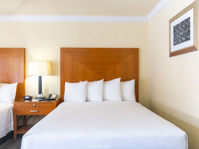 A hotel room with a double bed, nightstand, and lamp.