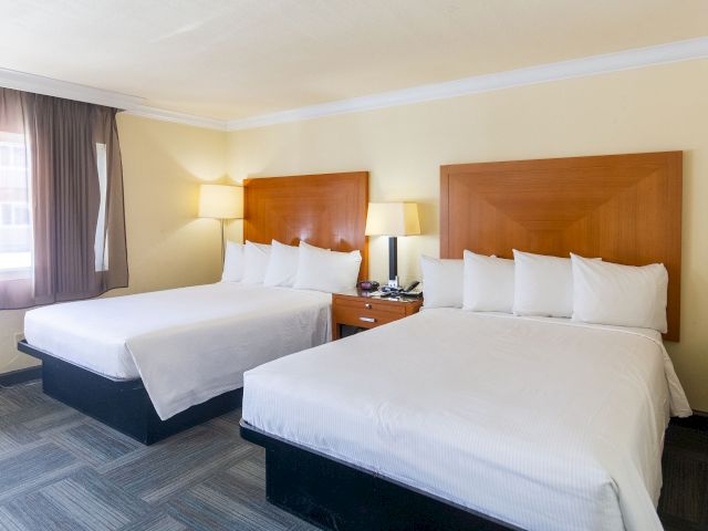 A hotel room with two beds, wooden headboards, and a nightstand between them.