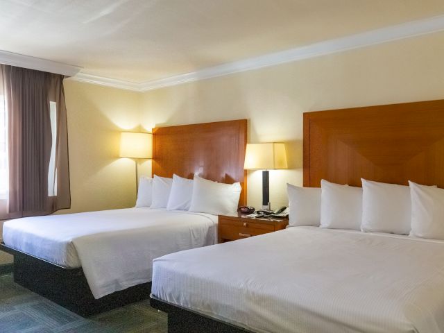 A hotel room with two beds, two lamps, a nightstand, and a window.