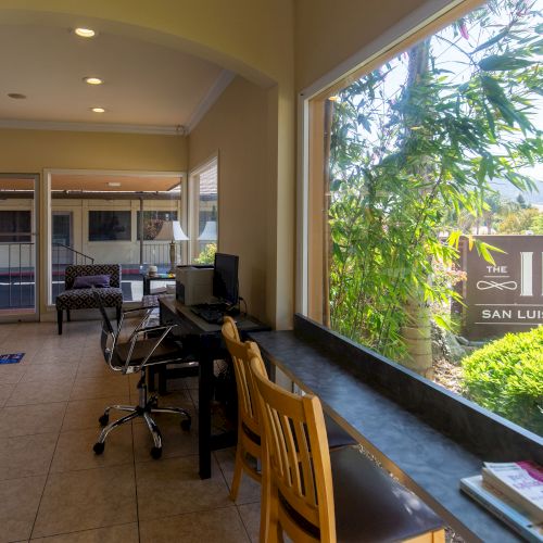 The image shows an indoor area with computers, chairs, and a large window with a sign outside reading 