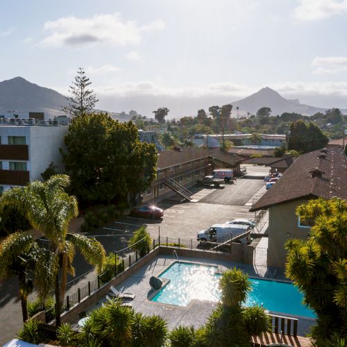 The image shows a residential area with a swimming pool, trees, parked cars, and mountains in the background under a partly cloudy sky.