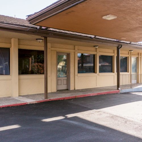 A building with a covered entrance, glass windows, a door, and a small ramp, likely a commercial or public facility, in daylight.