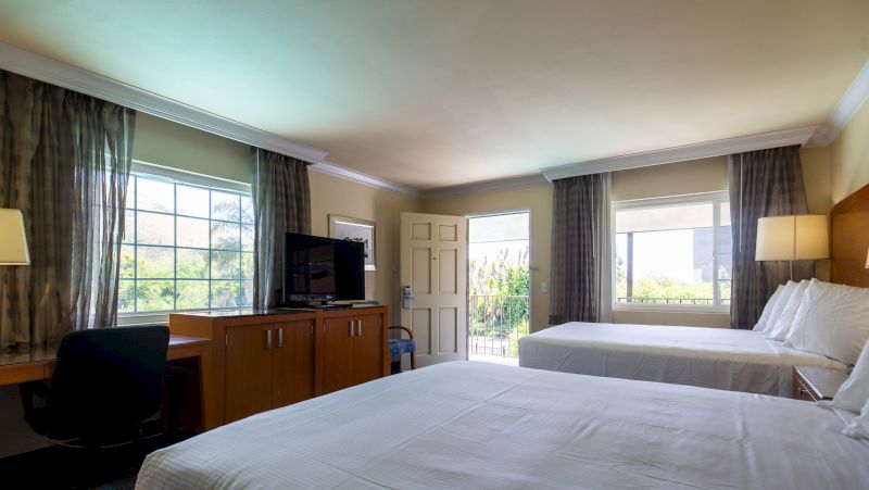 a hotel room with two beds, a desk, a tv, and a door