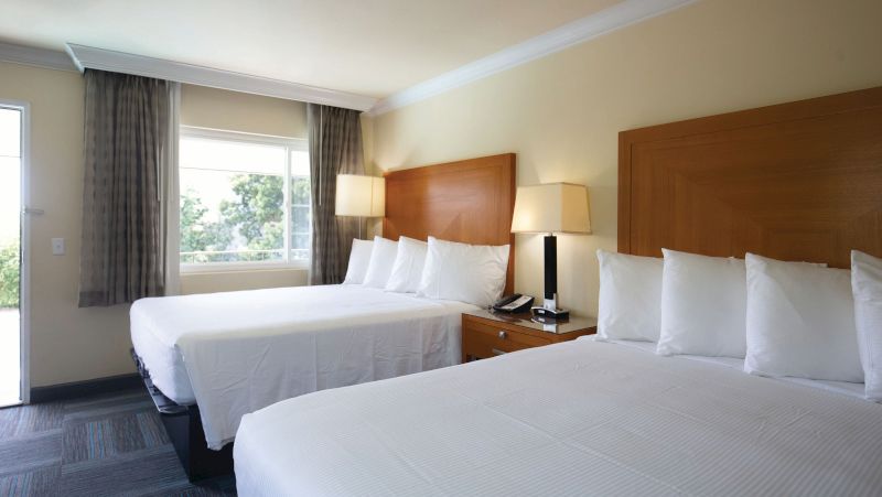 A hotel room with two beds, a nightstand, lamps, and a window