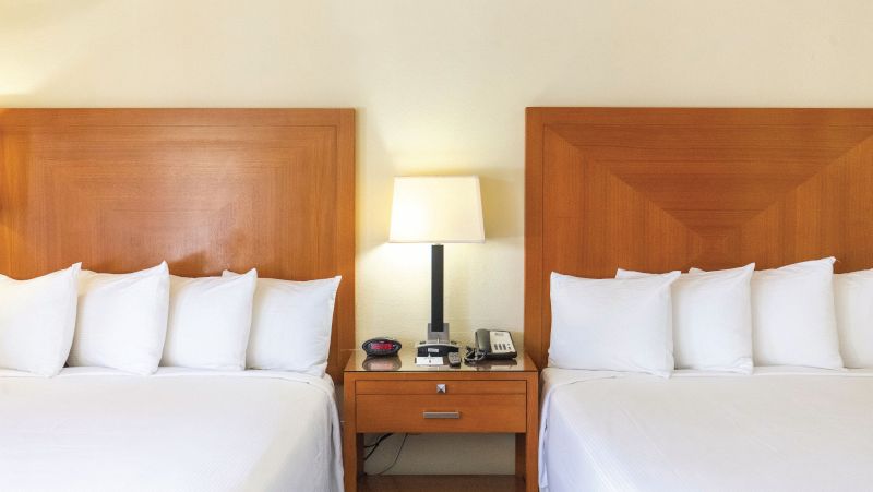 A hotel room with two double beds, wooden headboards, and white linens.