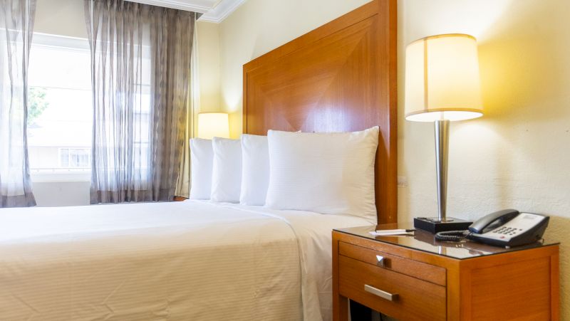 a hotel room with a bed, nightstand, and window