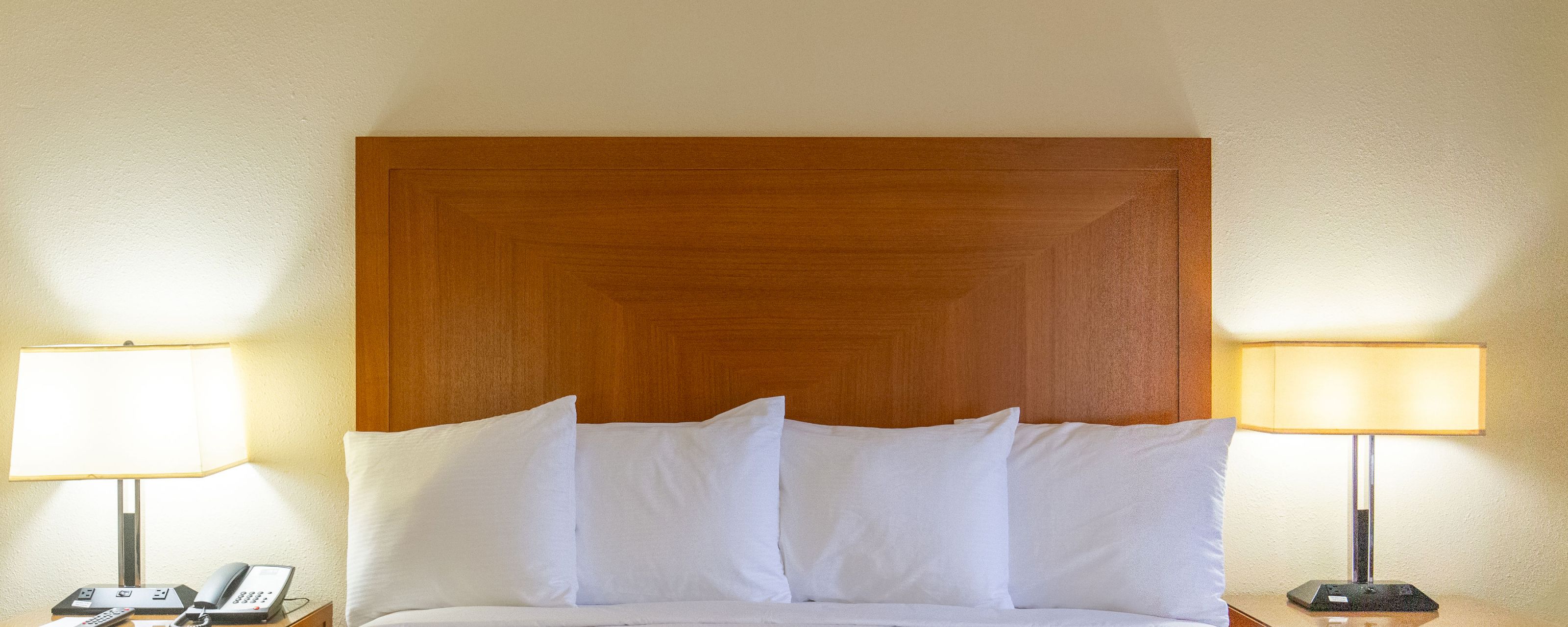A bed with white pillows and a wooden headboard flanked by two lamps
