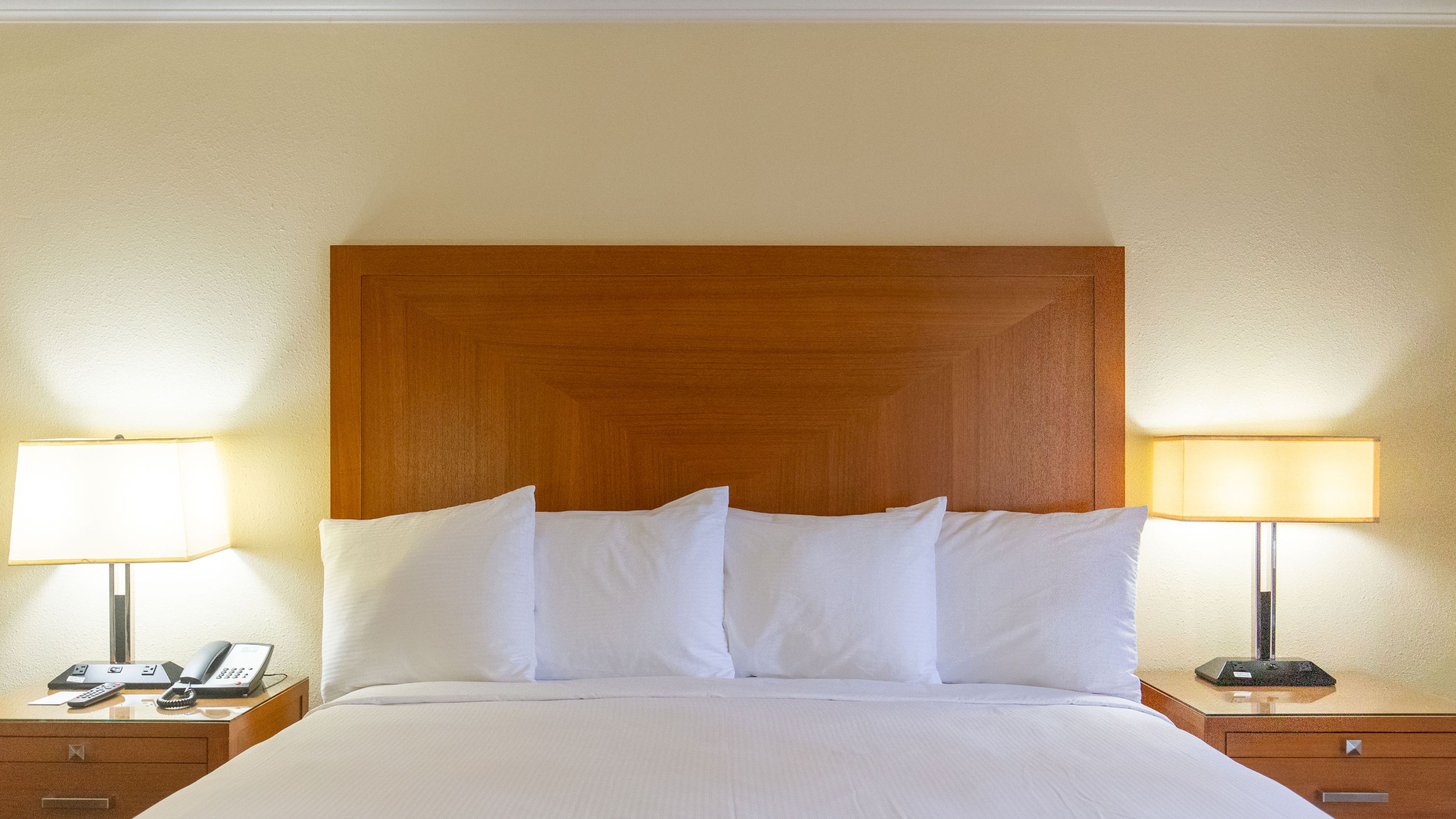 A neatly made bed with white pillows and sheets, flanked by two nightstands with lamps.