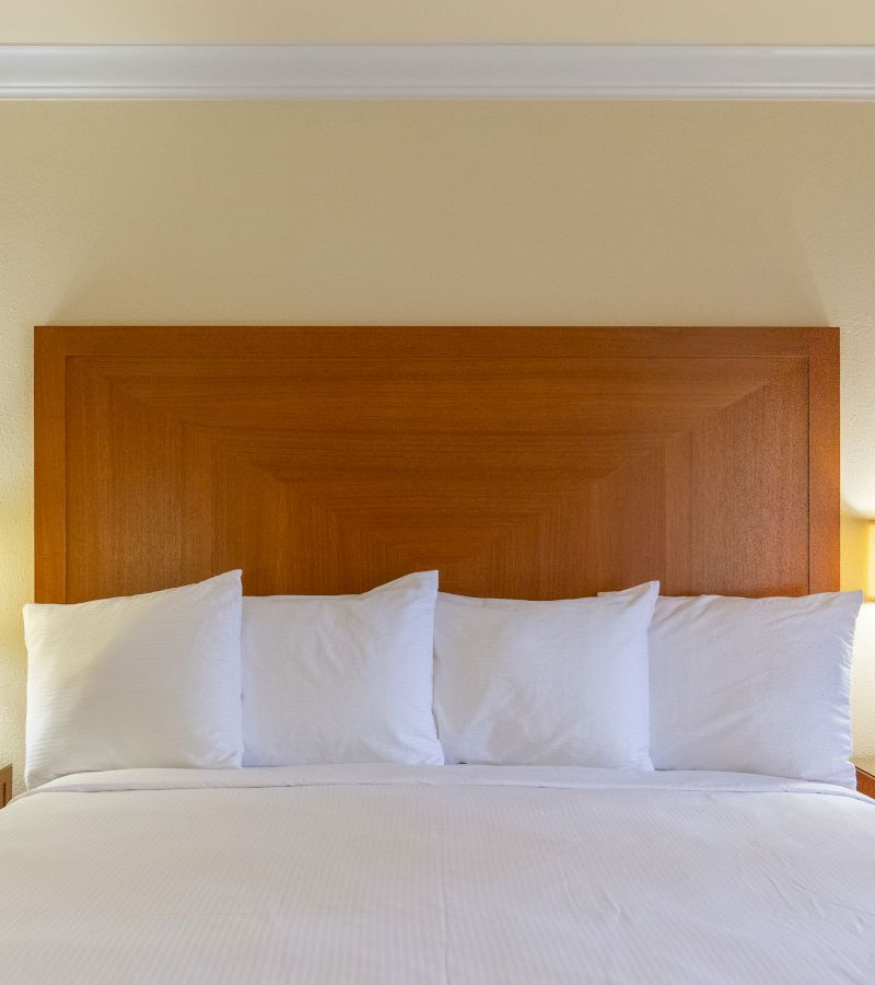 A close-up of a bed with a wooden headboard, white pillows, and white bedding.