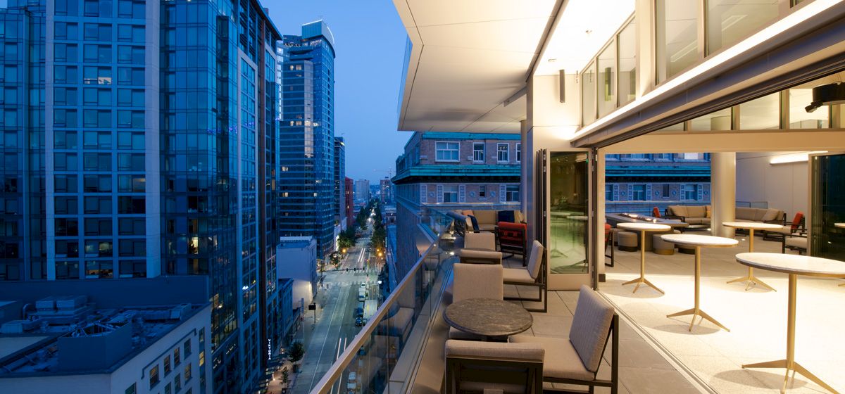 A balcony with seating area overlooking a city street at dusk.