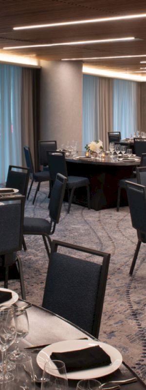 The image shows an elegant dining room with round tables set with glasses, plates, and napkins. The room is dimly lit with blue curtains.