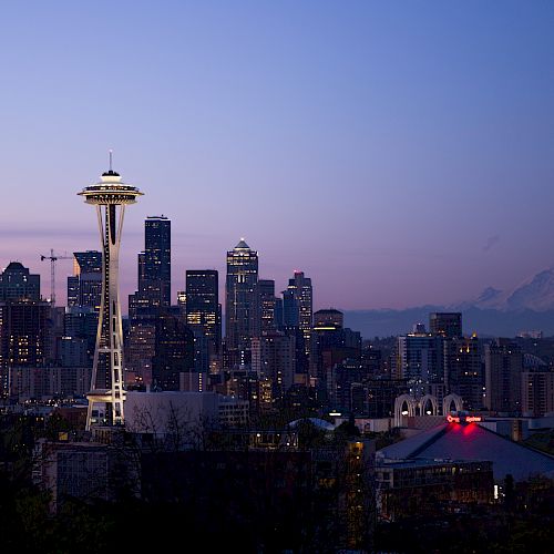 This image shows the city skyline of Seattle at dusk, featuring the Space Needle prominently with Mount Rainier visible in the background.